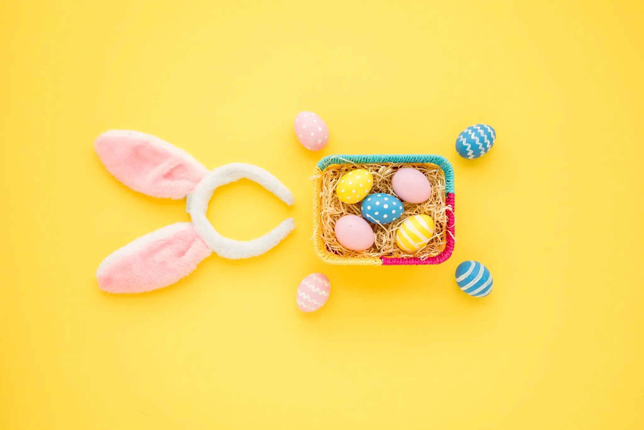 Ovos coloridos de Páscoa com orelhas de coelho em fundo amarelo, simbolizando a alegria da data.