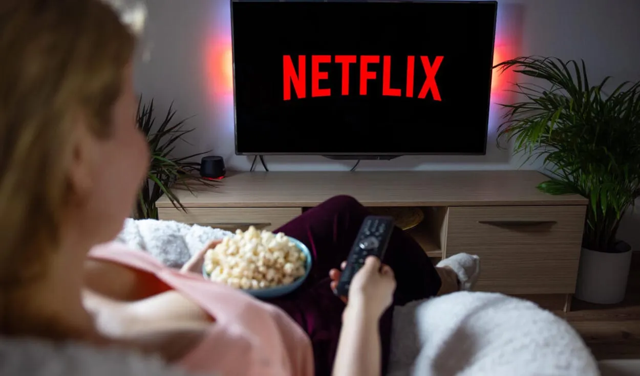 Pessoa assistindo à Netflix em uma TV, com pipoca na mão e controle remoto