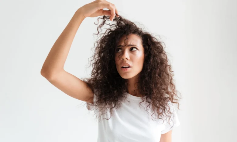 Mulher com cabelo cacheado, olhando atentamente para os fios, refletindo sobre o estilo do cabelo.
