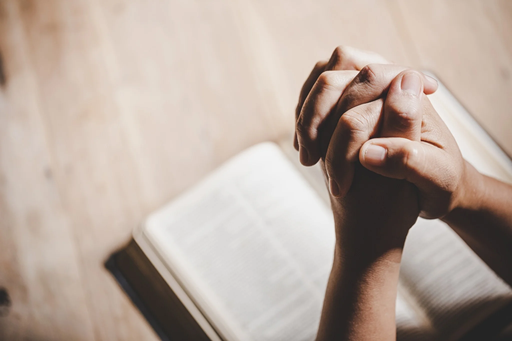 Mãos unidas em oração sobre um livro sagrado, simbolizando mensagens de reflexão e espiritualidade em feriados religiosos.
