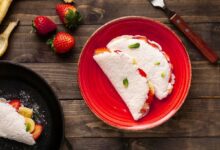 Tapioca com banana e morango servida em prato vermelho sobre mesa rústica