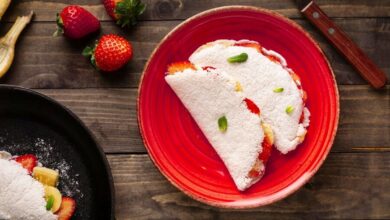 Tapioca com banana e morango servida em prato vermelho sobre mesa rústica
