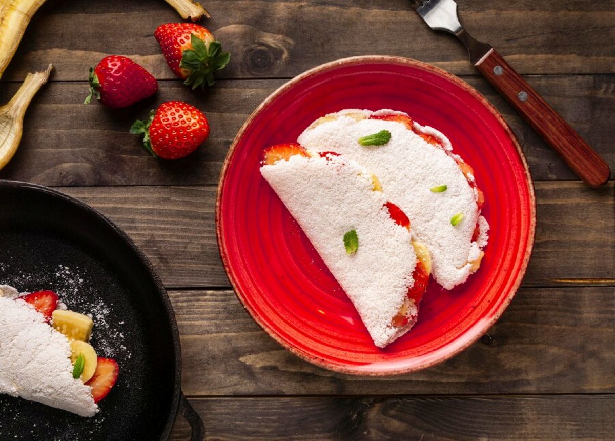 Tapioca com banana e morango servida em prato vermelho sobre mesa rústica