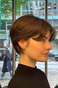 Mulher de perfil com corte pixie clássico, fios castanhos lisos e visual elegante.