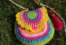 Bolsinha colorida de crochê com detalhes em pink, amarelo e verde, com botão e tassel.