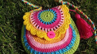 Bolsinha colorida de crochê com detalhes em pink, amarelo e verde, com botão e tassel.