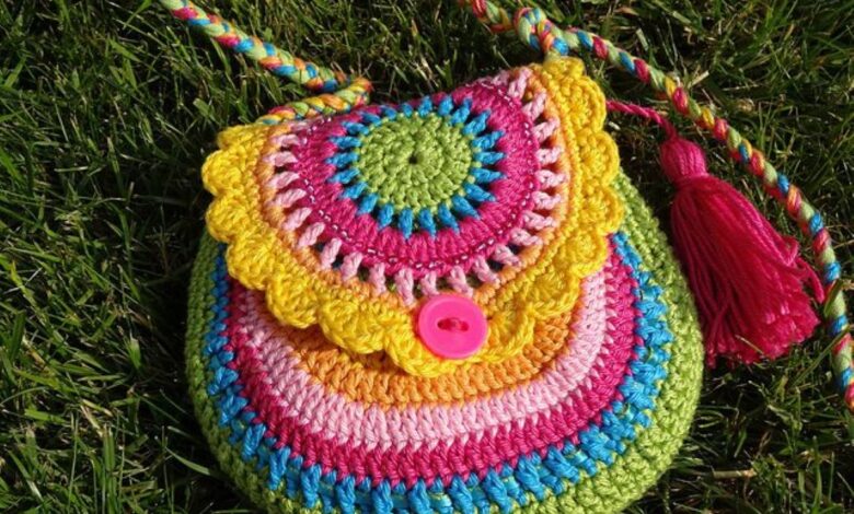 Bolsinha colorida de crochê com detalhes em pink, amarelo e verde, com botão e tassel.