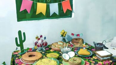 Mesa decorada para festa junina com toalha floral, comidas típicas e bandeirolas coloridas.