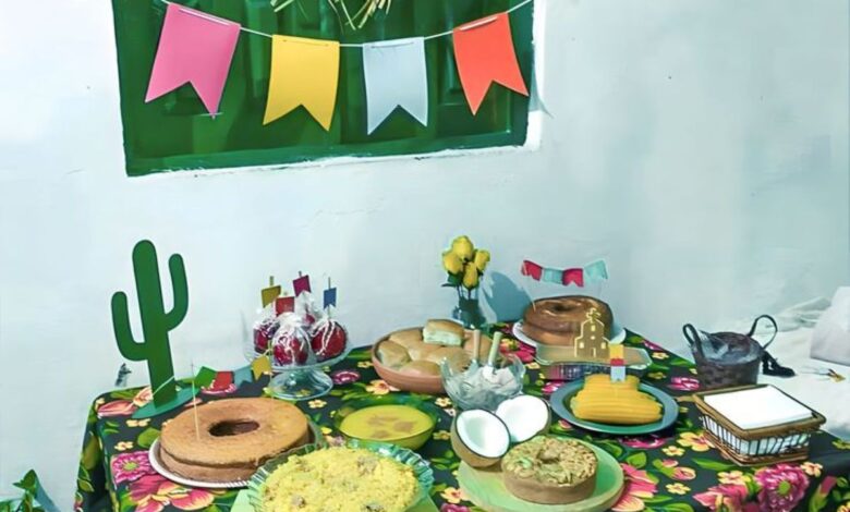 Mesa decorada para festa junina com toalha floral, comidas típicas e bandeirolas coloridas.