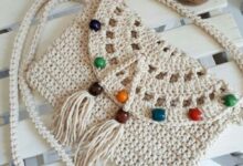 Bolsa de crochê artesanal com alça longa e miçangas coloridas sobre superfície de madeira branca