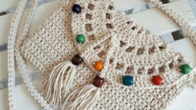 Bolsa de crochê artesanal com alça longa e miçangas coloridas sobre superfície de madeira branca