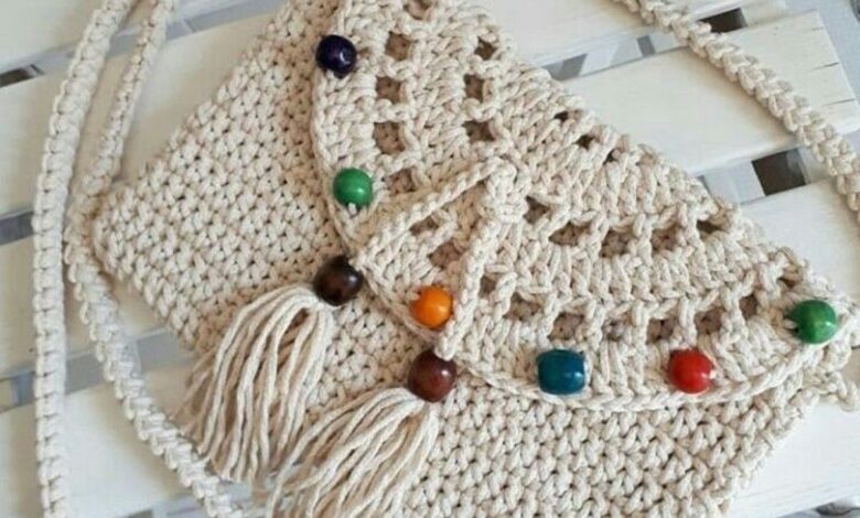 Bolsa de crochê artesanal com alça longa e miçangas coloridas sobre superfície de madeira branca