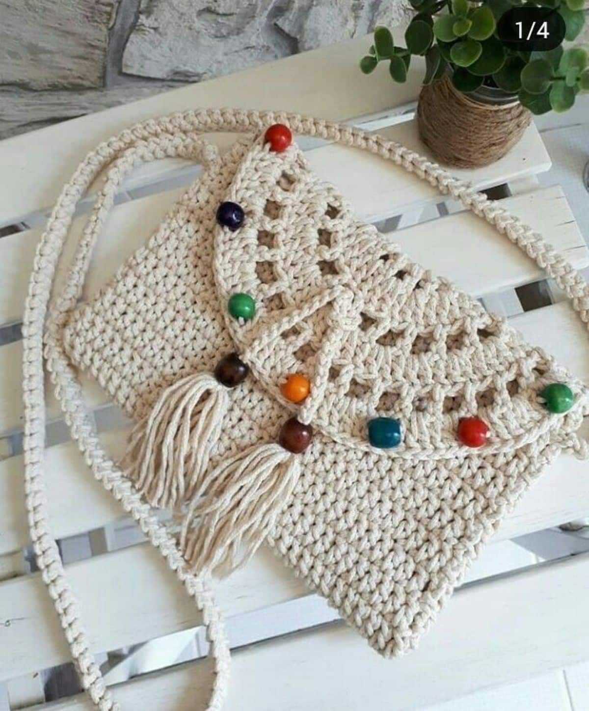 Bolsa de crochê artesanal com alça longa e miçangas coloridas sobre superfície de madeira branca