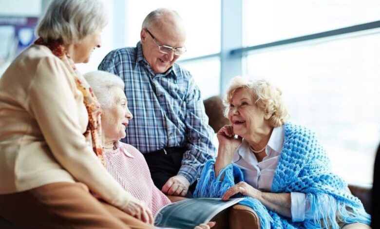 Grupo de idosos sorrindo e conversando em um ambiente claro e acolhedor, compartilhando momentos de amizade e cumplicidade.