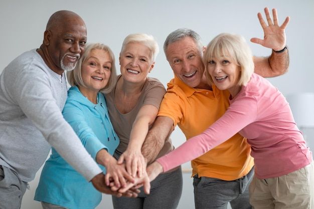 Grupo diverso de idosos unindo as mãos com sorrisos de amizade e companheirismo, celebrando a união e o apoio mútuo.