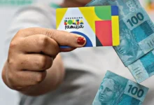 Cartão do Programa Bolsa Família com cédulas de 100 reais ao fundo
