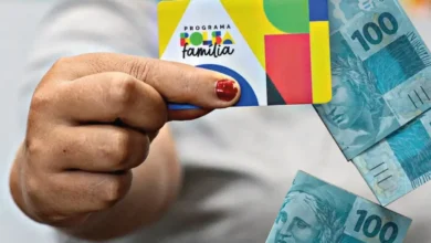Cartão do Programa Bolsa Família com cédulas de 100 reais ao fundo