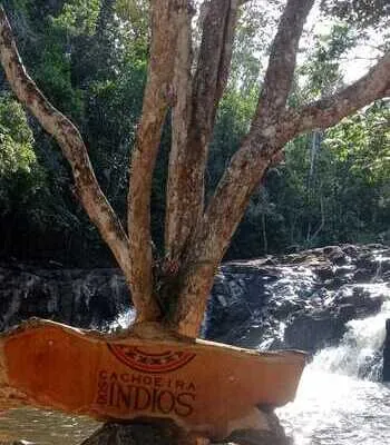 Placa de identificação da Cachoeira dos Índios, com uma árvore ao lado e águas caindo em um cenário natural de Subaúma, perto de Salvador
