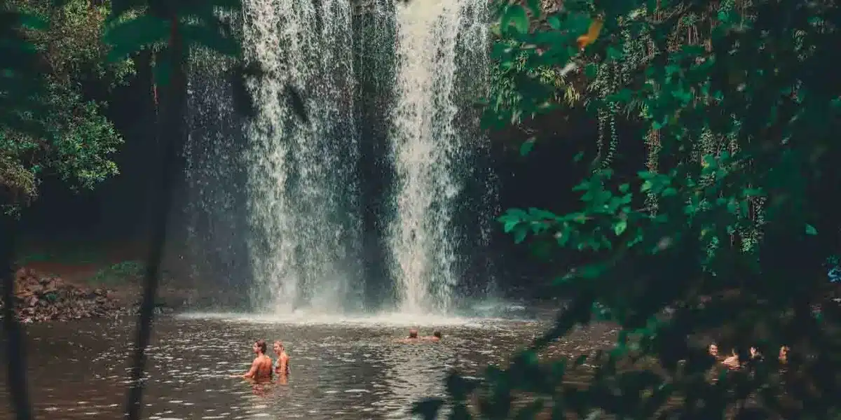 Pessoas se banhando na base de uma cachoeira rodeada por vegetação em uma área próxima a Salvador