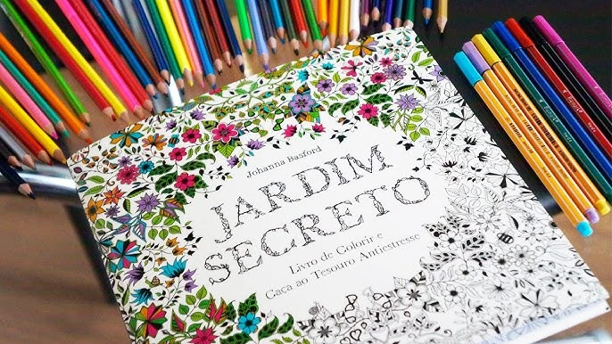 Livro Jardim Secreto com desenhos para colorir, cercado por lápis de cor e canetinhas