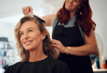 Mulher madura sorrindo enquanto tem o cabelo escovado por cabeleireira em salão de beleza