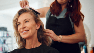Mulher madura sorrindo enquanto tem o cabelo escovado por cabeleireira em salão de beleza
