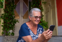 Mulher sorridente usando o celular sentada em frente à sua casa.