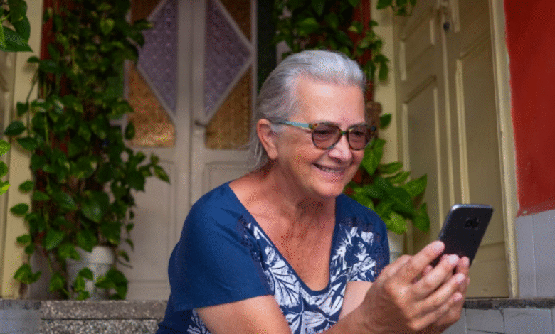 Mulher sorridente usando o celular sentada em frente à sua casa.