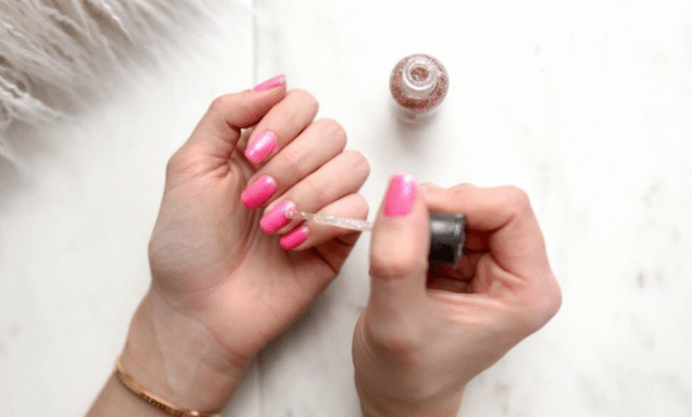 Mulher aplicando esmalte com brilho sobre unhas rosa em um momento de cuidado pessoal