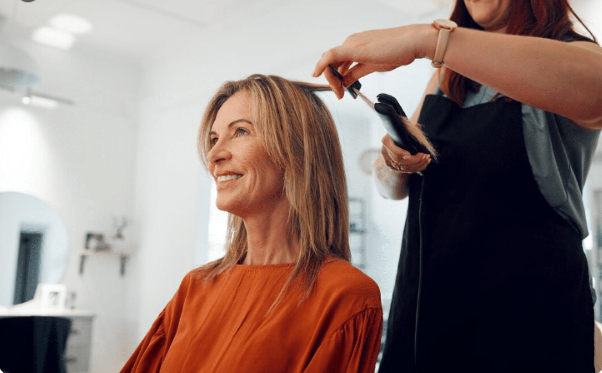 Mulher sorrindo enquanto recebe penteado no salão, corte Riviera Bob em destaque, simbolizando a tendência de cabelo em 2025.