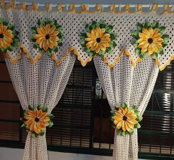 Cortinas de crochê brancas com detalhes em flores amarelas e verdes, decorando janela.