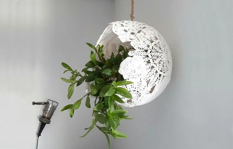 Luminária pendente com crochê endurecido branco e plantas verdes na decoração