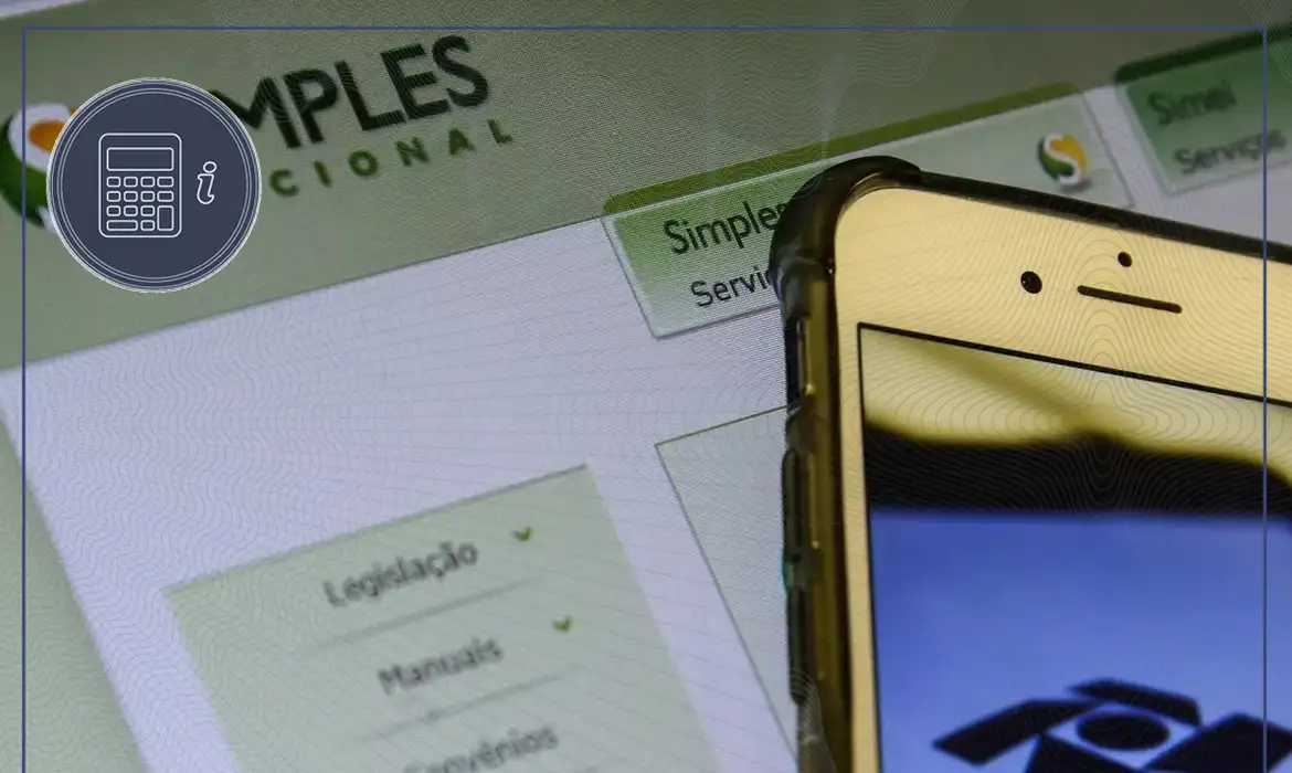 Smartphone exibindo o aplicativo MEI com o site do Simples Nacional ao fundo em um monitor.