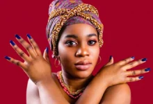 Mulher negra usando turbante colorido e esmalte azul escuro nas unhas, destacando tons de pele e cores que valorizam as mãos.pele negra