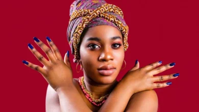 Mulher negra usando turbante colorido e esmalte azul escuro nas unhas, destacando tons de pele e cores que valorizam as mãos.pele negra