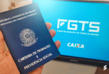 Carteira de trabalho sendo segurada com a tela de fundo mostrando o logo do FGTS e CAIXA