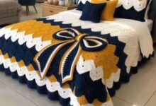 Jogo de cama em crochê nas cores azul, mostarda e branco com laço decorativo sobre a cama.