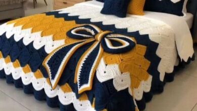 Jogo de cama em crochê nas cores azul, mostarda e branco com laço decorativo sobre a cama.