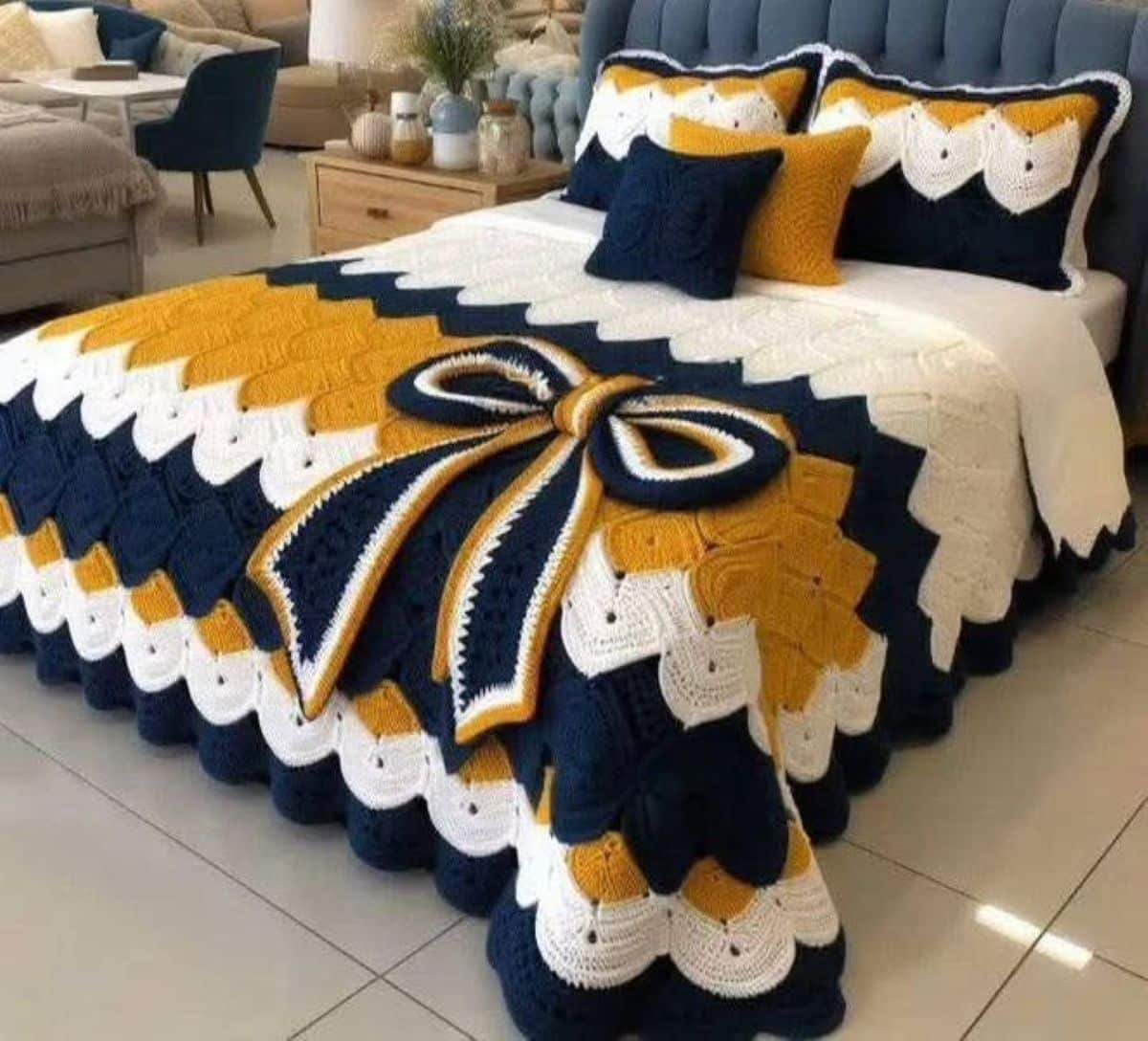 Jogo de cama em crochê nas cores azul, mostarda e branco com laço decorativo sobre a cama.