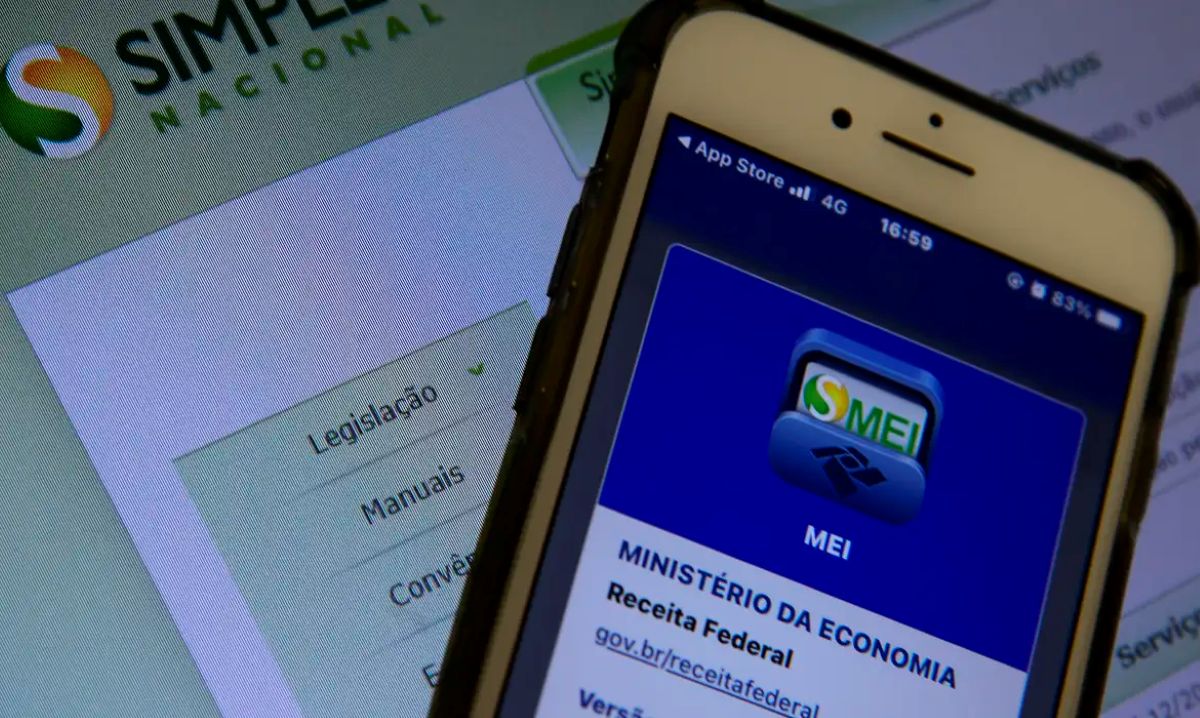 Smartphone com o aplicativo MEI aberto em primeiro plano e o site do Simples Nacional ao fundo.