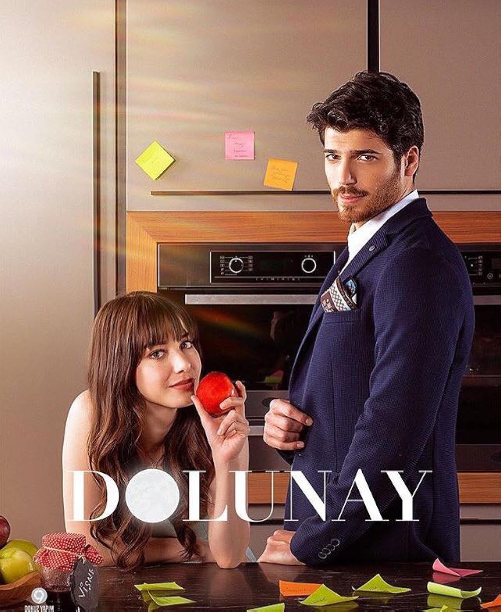 Cena da novela turca "Dolunay" Casal da novela turca "Dolunay" em um momento descontraído na cozinha, com a mulher segurando uma maçã e o homem ao seu lado.