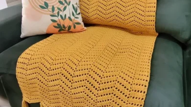 Manta de crochê amarela com franjas sobre sofá verde e almofada decorativa com estampa moderna.