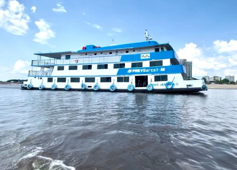 Embarcação PREVBarco navegando em águas calmas perto de comunidade ribeirinha.