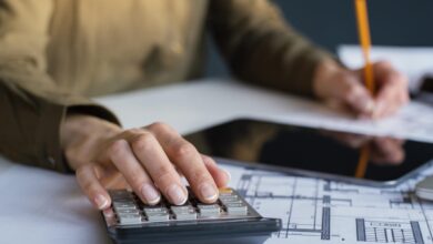 Mulher trabalhando em escritório com plantas de construção e calculadora, representando planejamento de retenção do INSS.