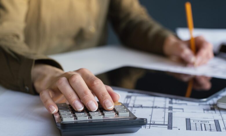 Mulher trabalhando em escritório com plantas de construção e calculadora, representando planejamento de retenção do INSS.