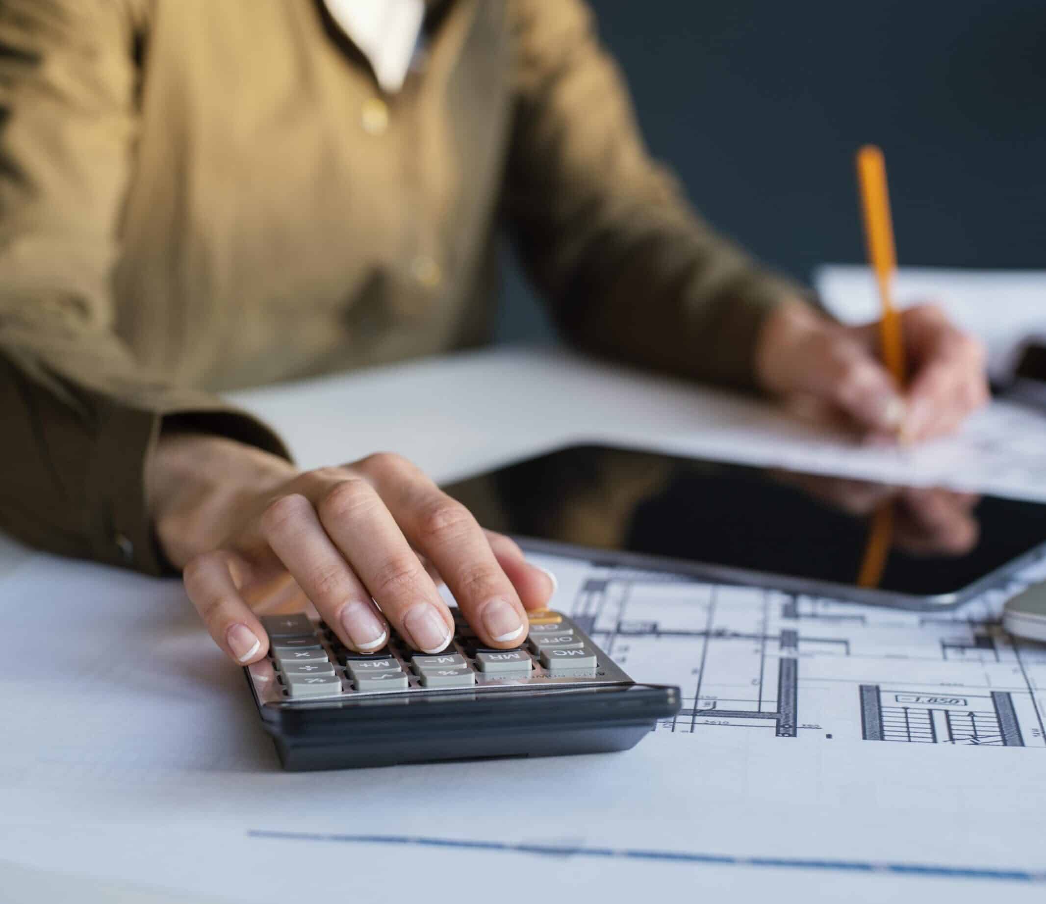 Mulher trabalhando em escritório com plantas de construção e calculadora, representando planejamento de retenção do INSS.