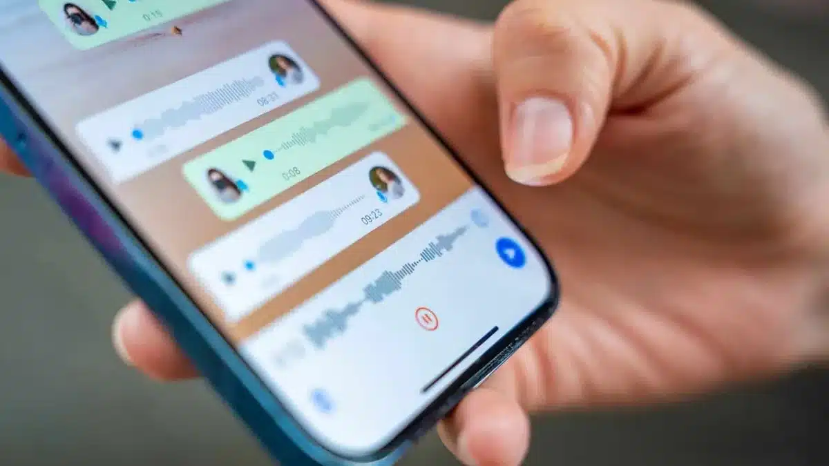Pessoa segurando um smartphone com a tela do WhatsApp mostrando mensagens de voz