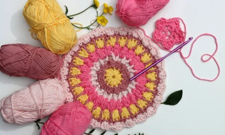 Detalhe de peça redonda em crochĂȘ colorido com fios rosa, amarelo e marrom ao redor, pronta para acabamento.