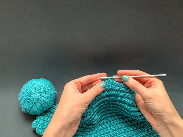 Mãos segurando agulha e trabalhando crochê em fio azul, mostrando técnica de acabamento.