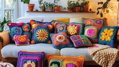Almofadas de crochê coloridas e detalhadas sobre sofá cinza em sala iluminada, com plantas ao fundo.